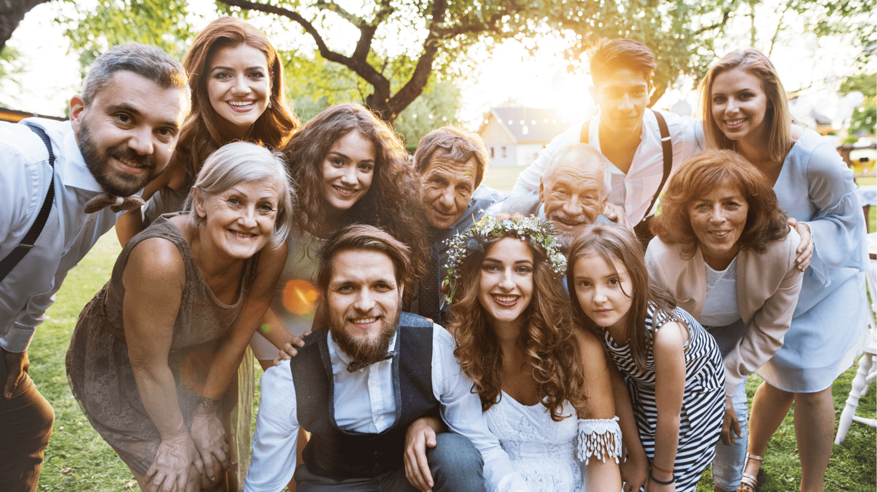A joyful group of family and friends gathers outdoors to celebrate a wedding.