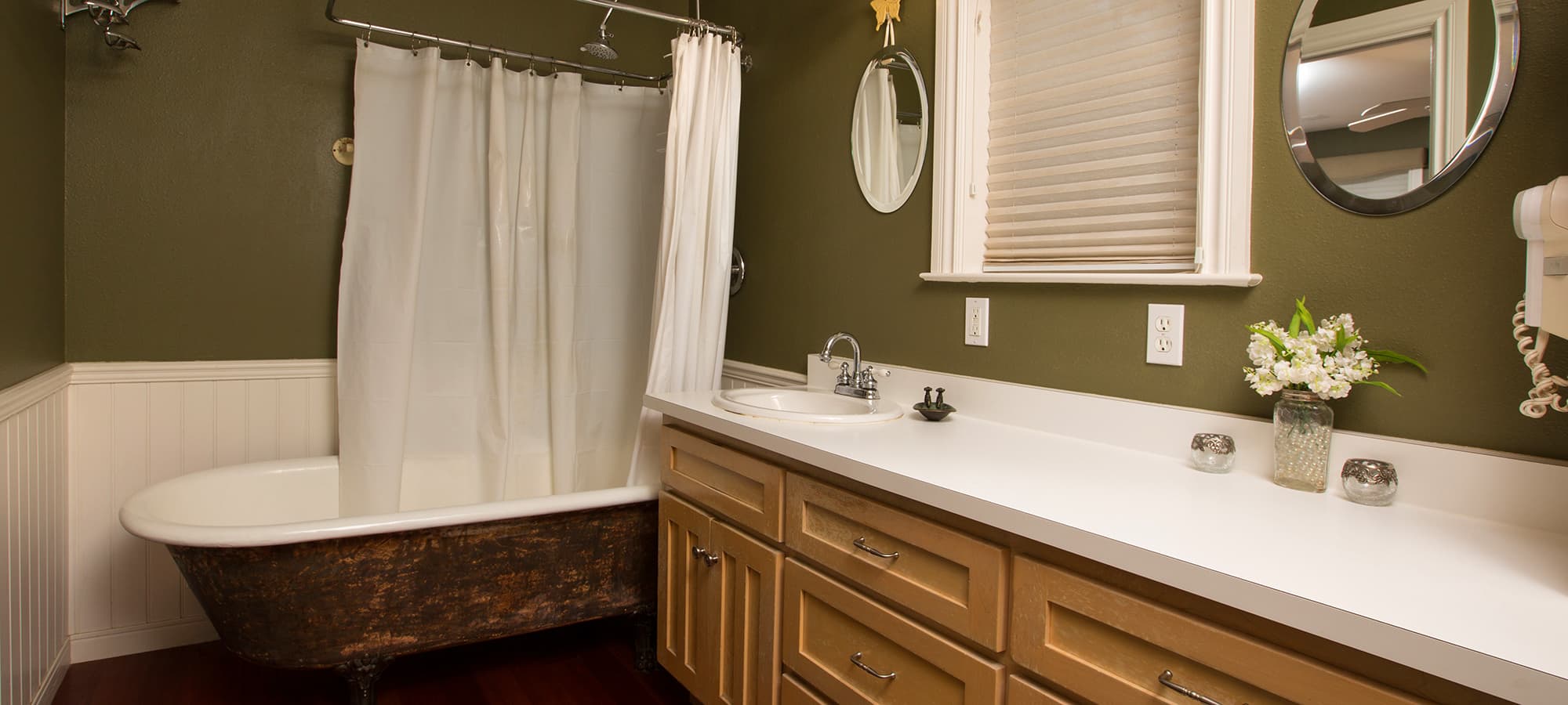 A stylish bathroom featuring a clawfoot tub, white shower curtain, and a vintage-inspired sink with wooden cabinetry.