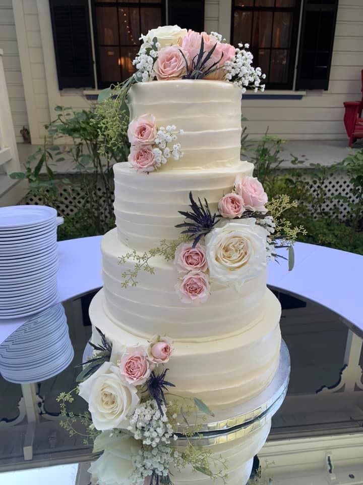 A three-tiered white wedding cake decorated with pink roses and greenery.