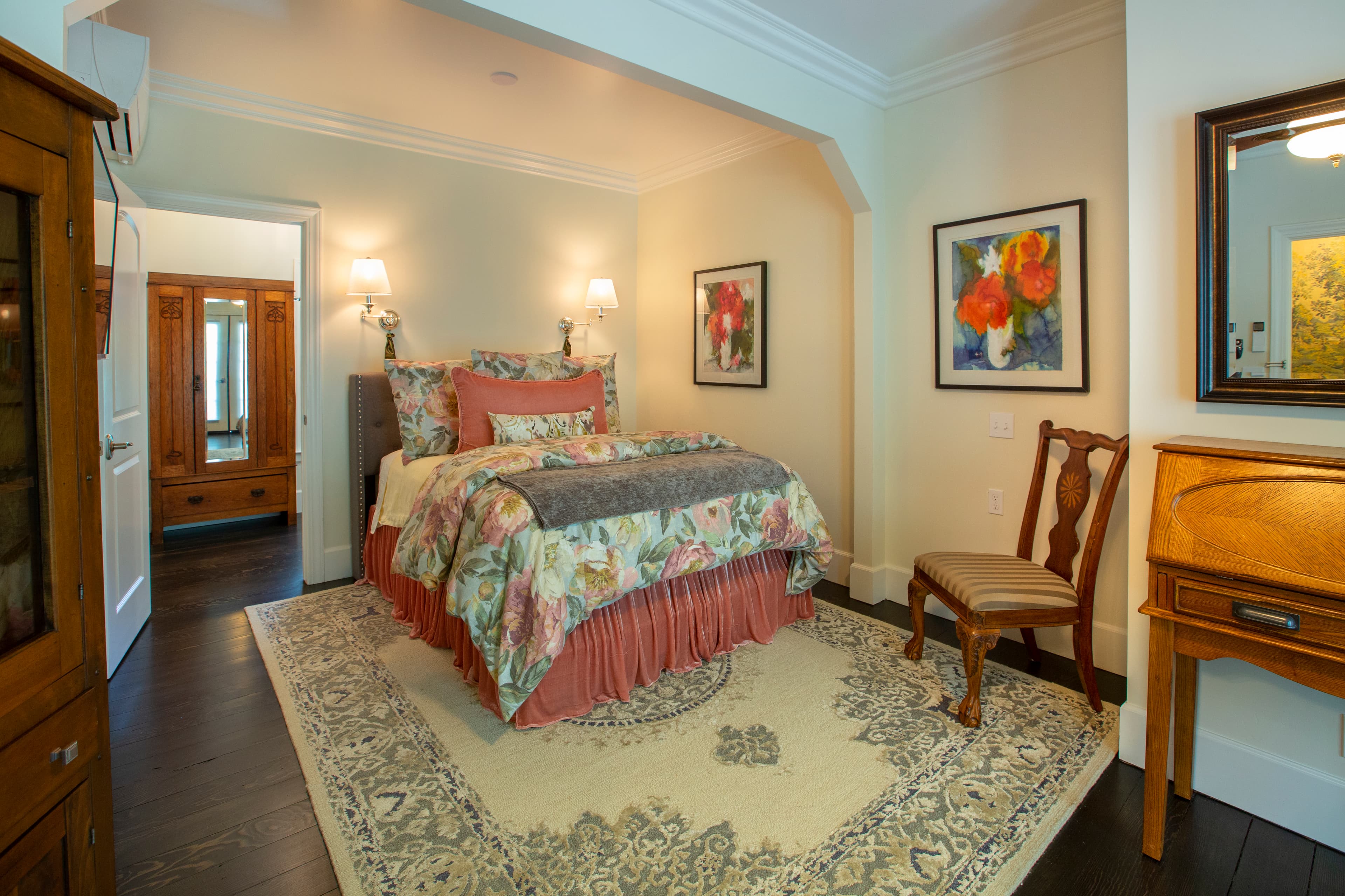 Cozy bedroom featuring a floral-patterned bedspread, wooden furniture, and artwork on the walls.
