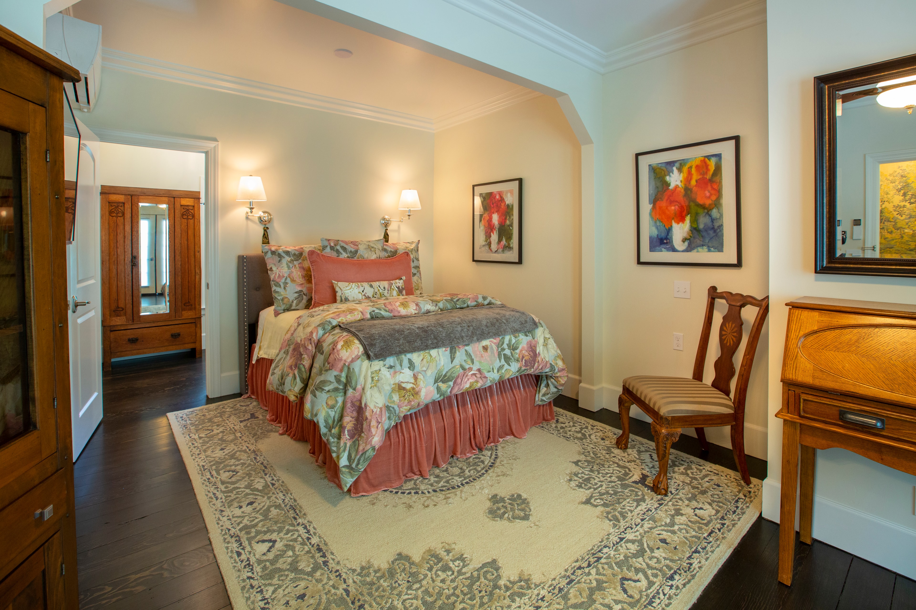 Cozy bedroom featuring a floral-patterned bedspread, wooden furniture, and artwork on the walls.