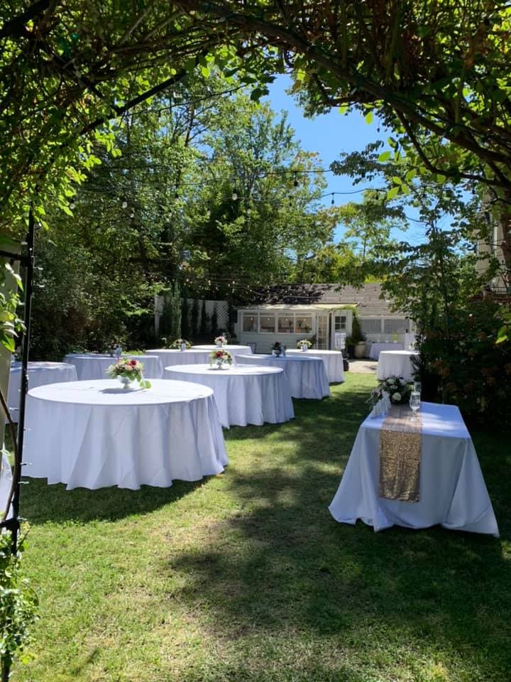 A sunny garden setting with several round tables draped in white linens and adorned with floral centerpieces.
