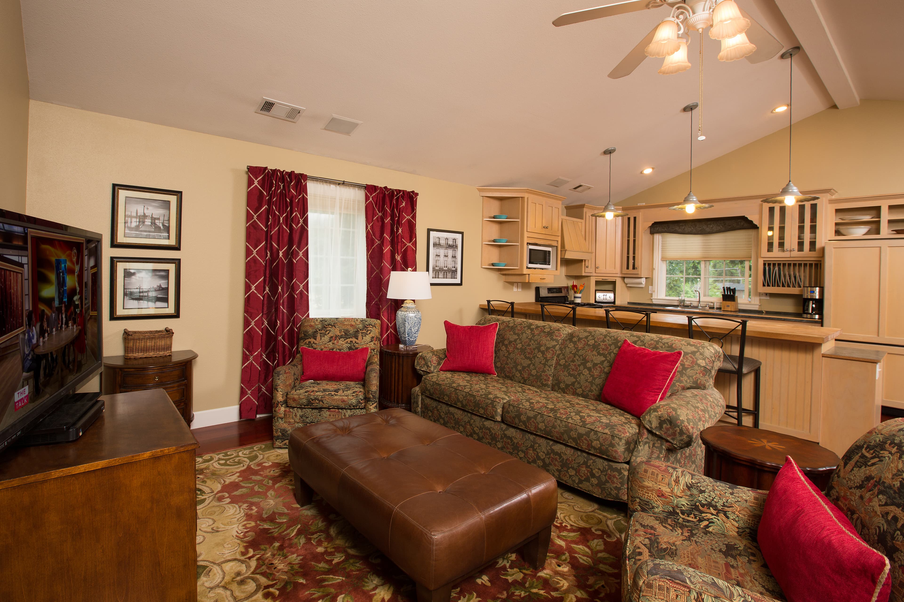 Cozy living room featuring floral-patterned furniture, bright red accents, and an open kitchen area.