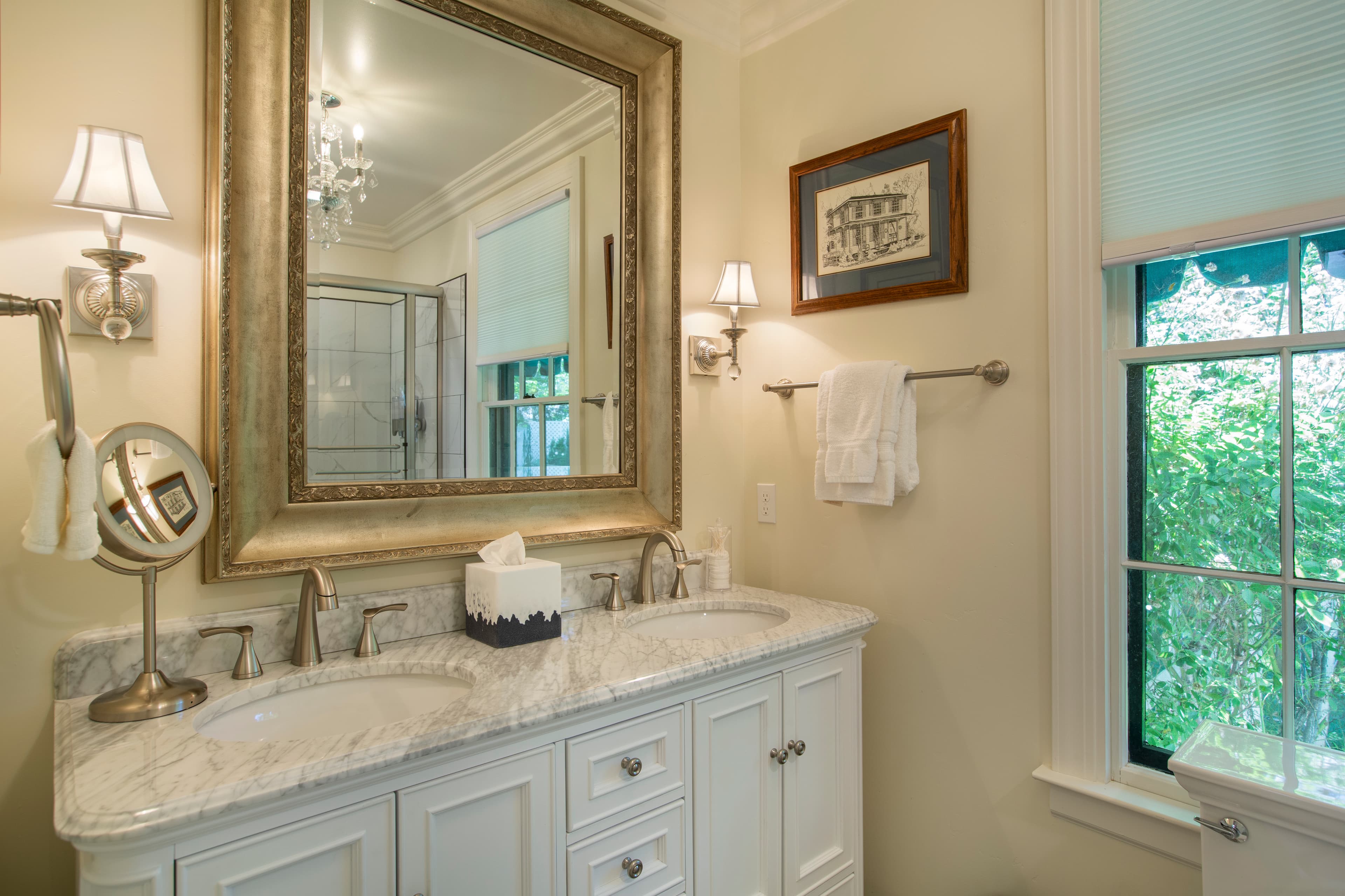 A stylish bathroom featuring a double sink vanity, ornate mirror, and natural light from a window.