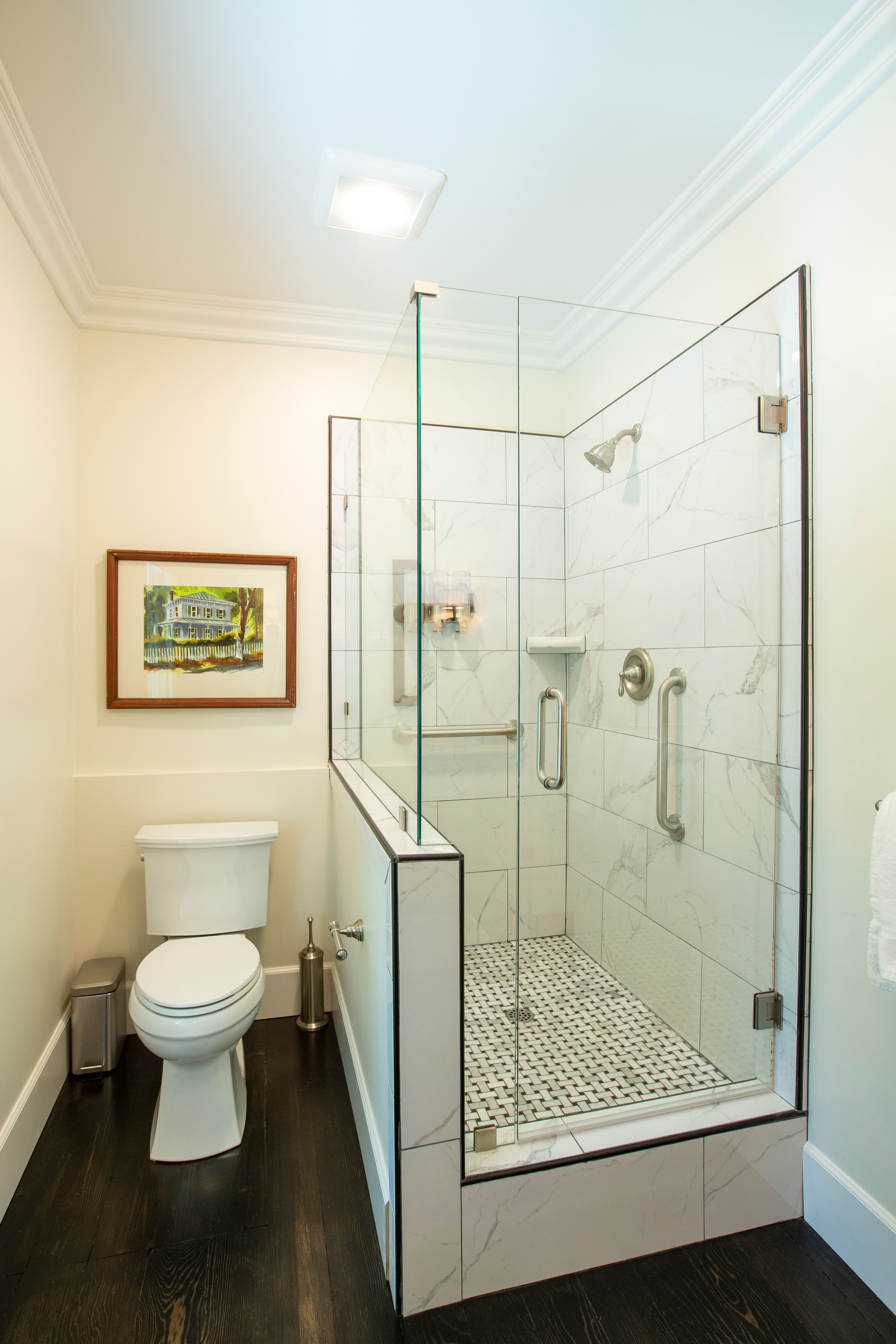 A modern bathroom featuring a glass shower, toilet, and framed artwork on the wall.