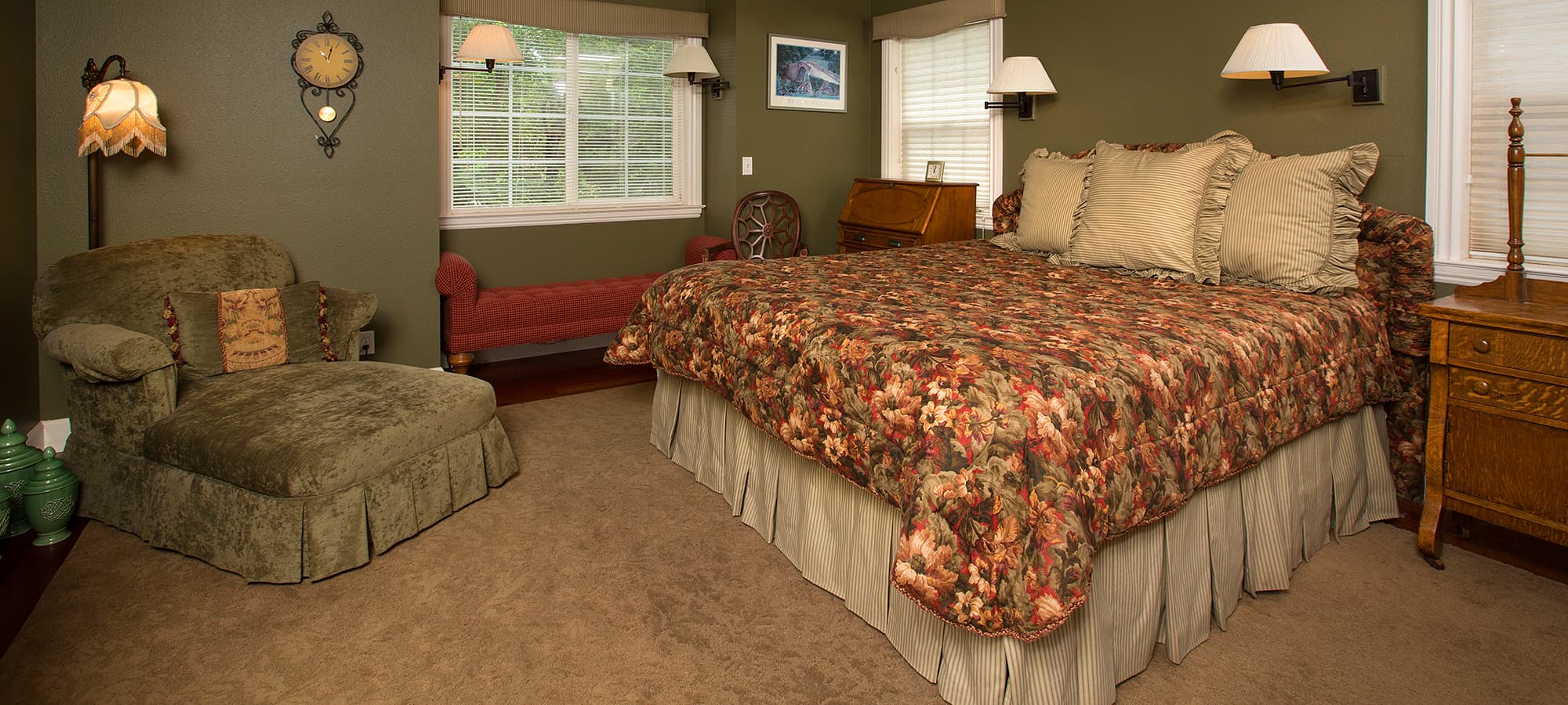 Cozy bedroom featuring a floral-patterned bedspread, a chaise lounge, and warm lighting.