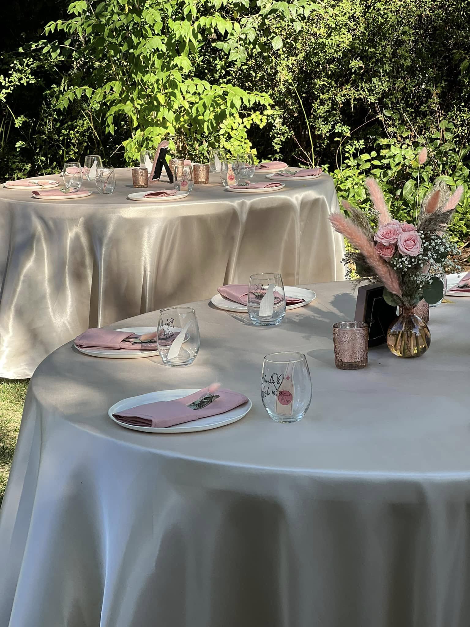 Elegant outdoor dining setup with two tables adorned with pink napkins, glasses, and floral arrangements.