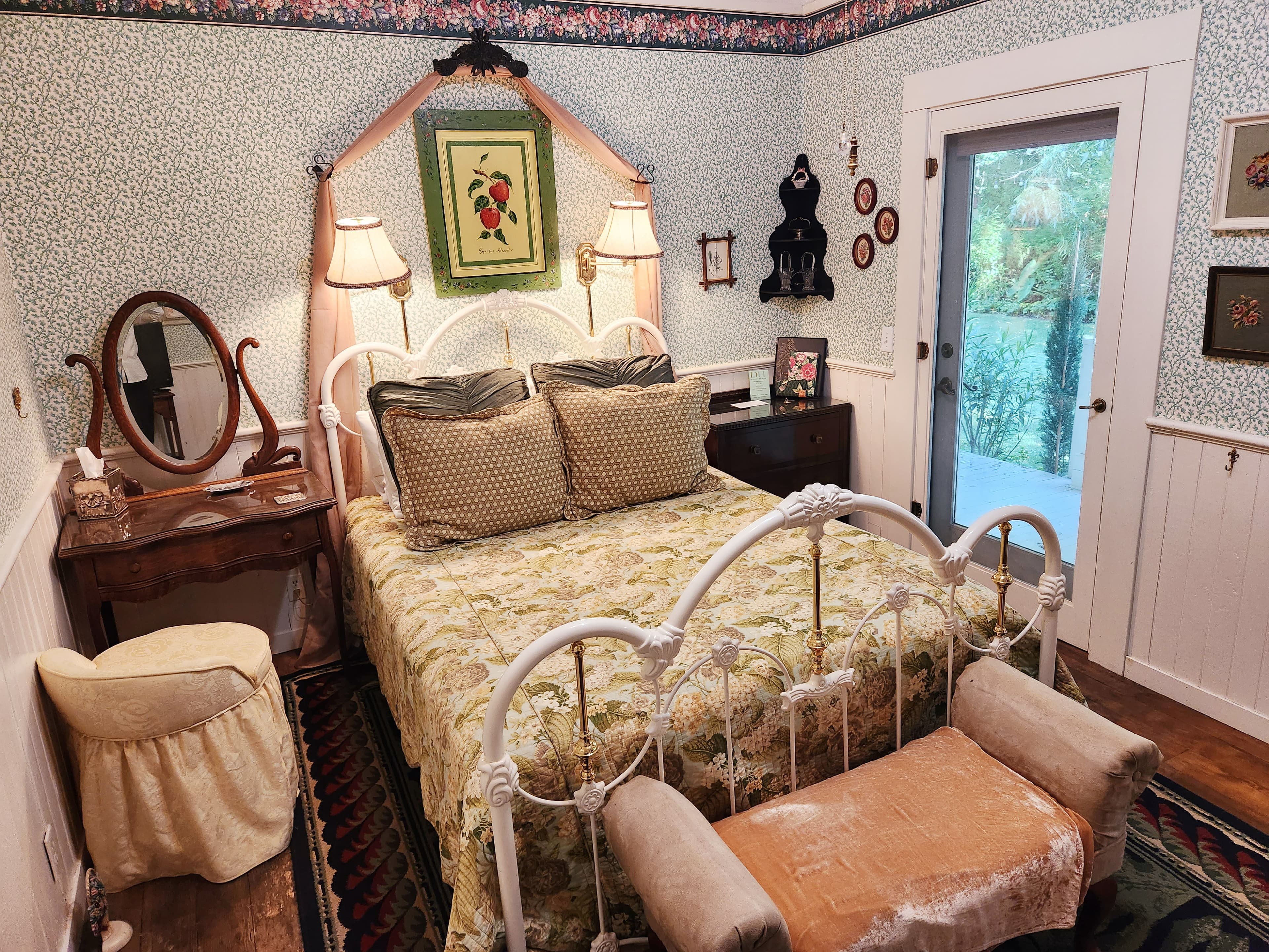 A cozy bedroom featuring a floral-patterned bedspread, vintage decor, and a door leading to a garden view.