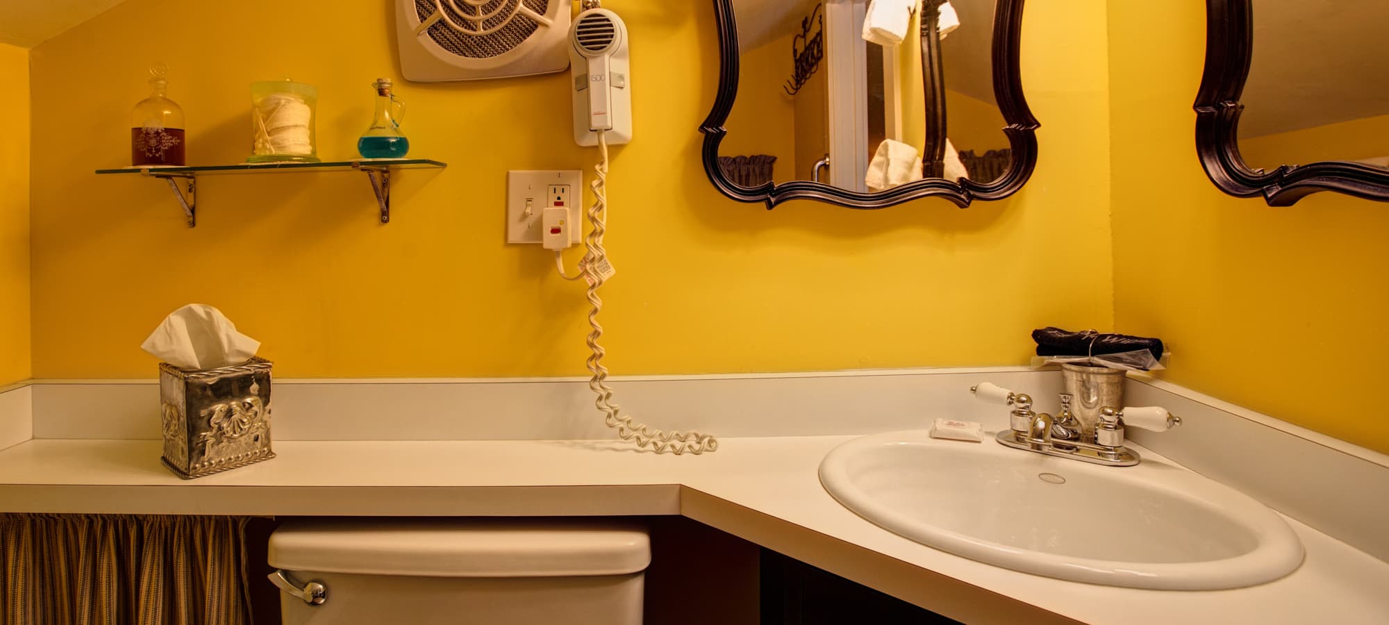 A bright yellow bathroom featuring a sink, toilet, wall mirror, and vintage telephone.