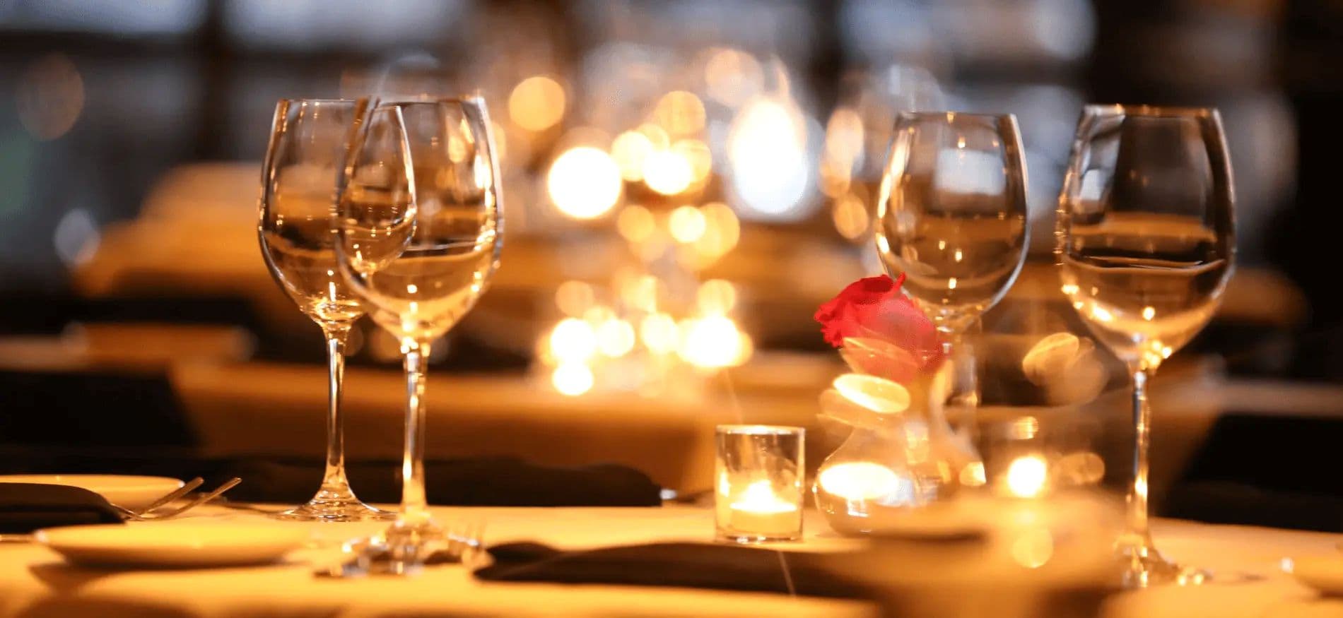 Wine glasses on a dimly lit table with candles and a rose. Wine glasses on a dimly lit table with candles and a rose.