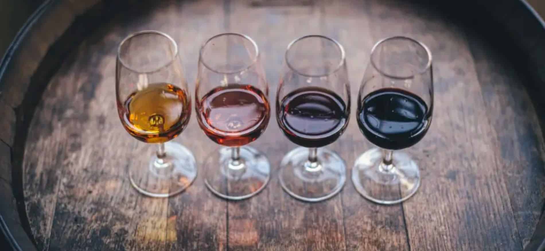 4 wine glasses lined up on top of a wine barrel with different types of wine in each glass. 4 wine glasses lined up on top of a wine barrel with different types of wine in each glass.